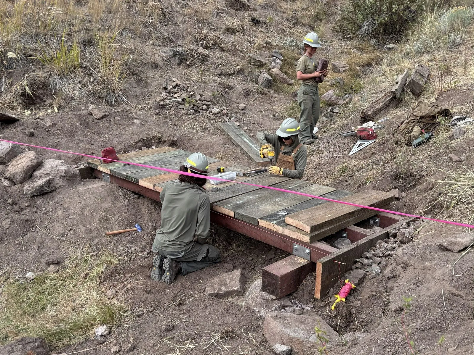 Three workers drill decking onto bridge stringers